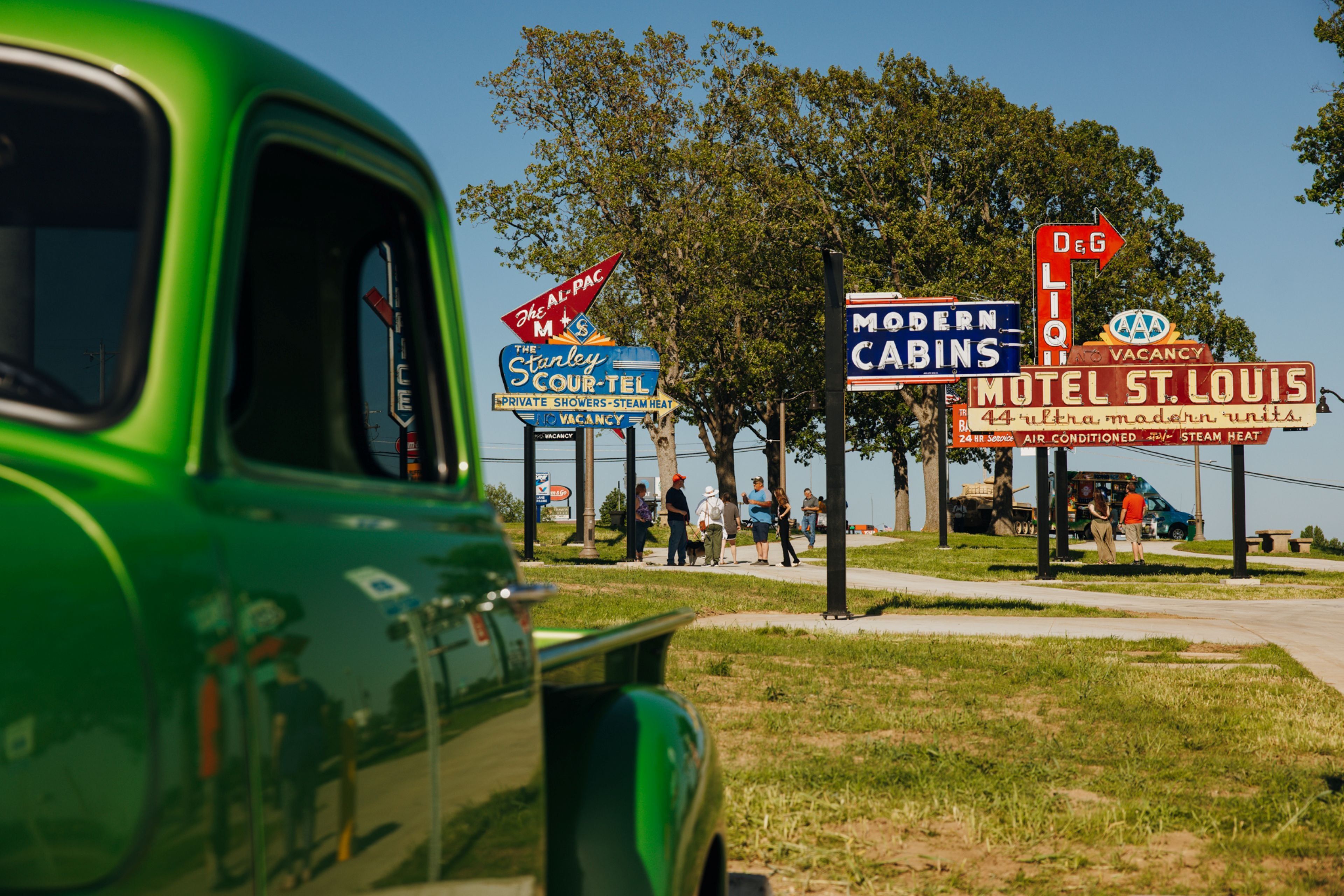 A vintage green car parked near a motel with signs advertising 'Modern Cabins' and 'Motel St. Louis'.