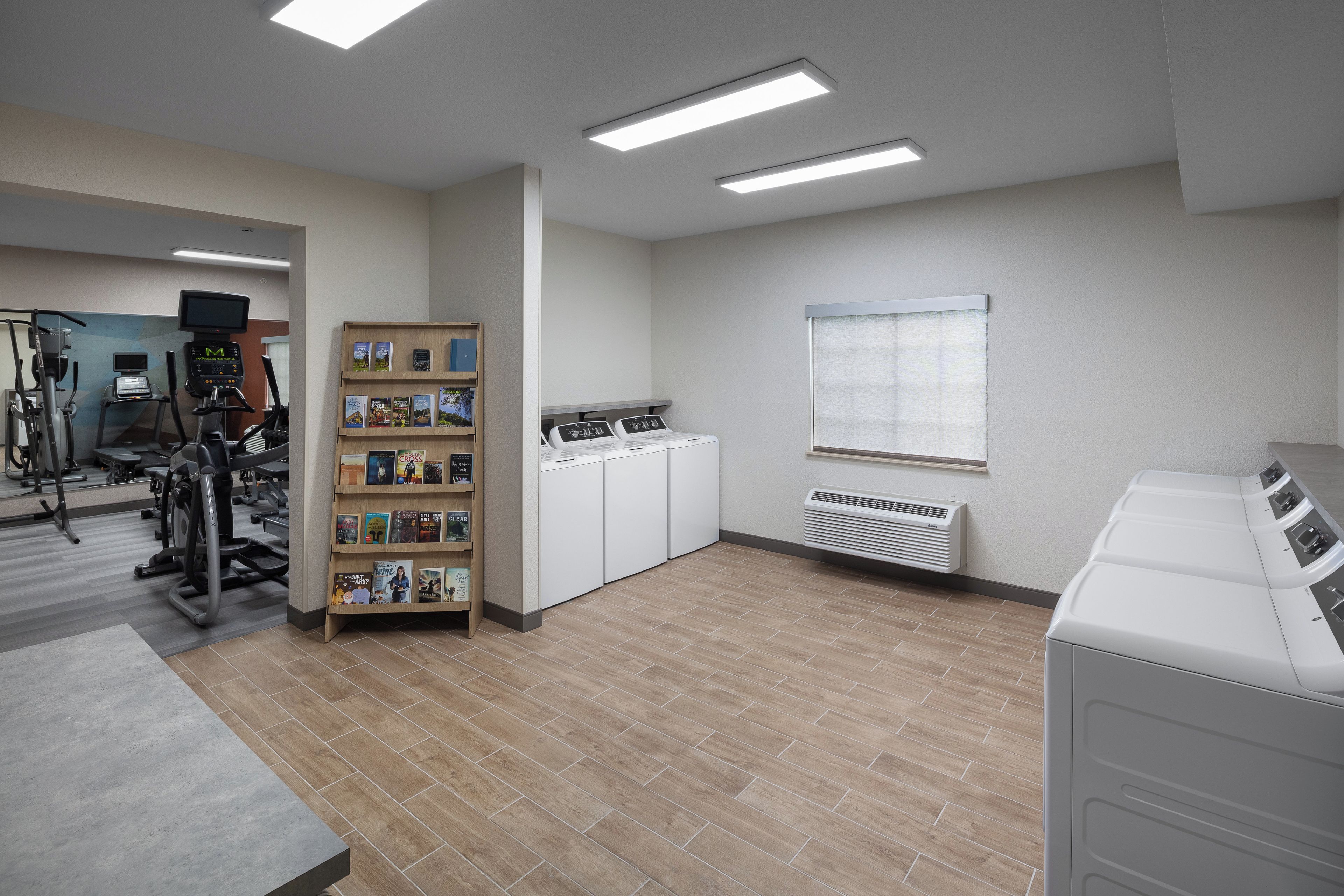A laundry room with a washing machine, dryer, and a bookcase with magazines.