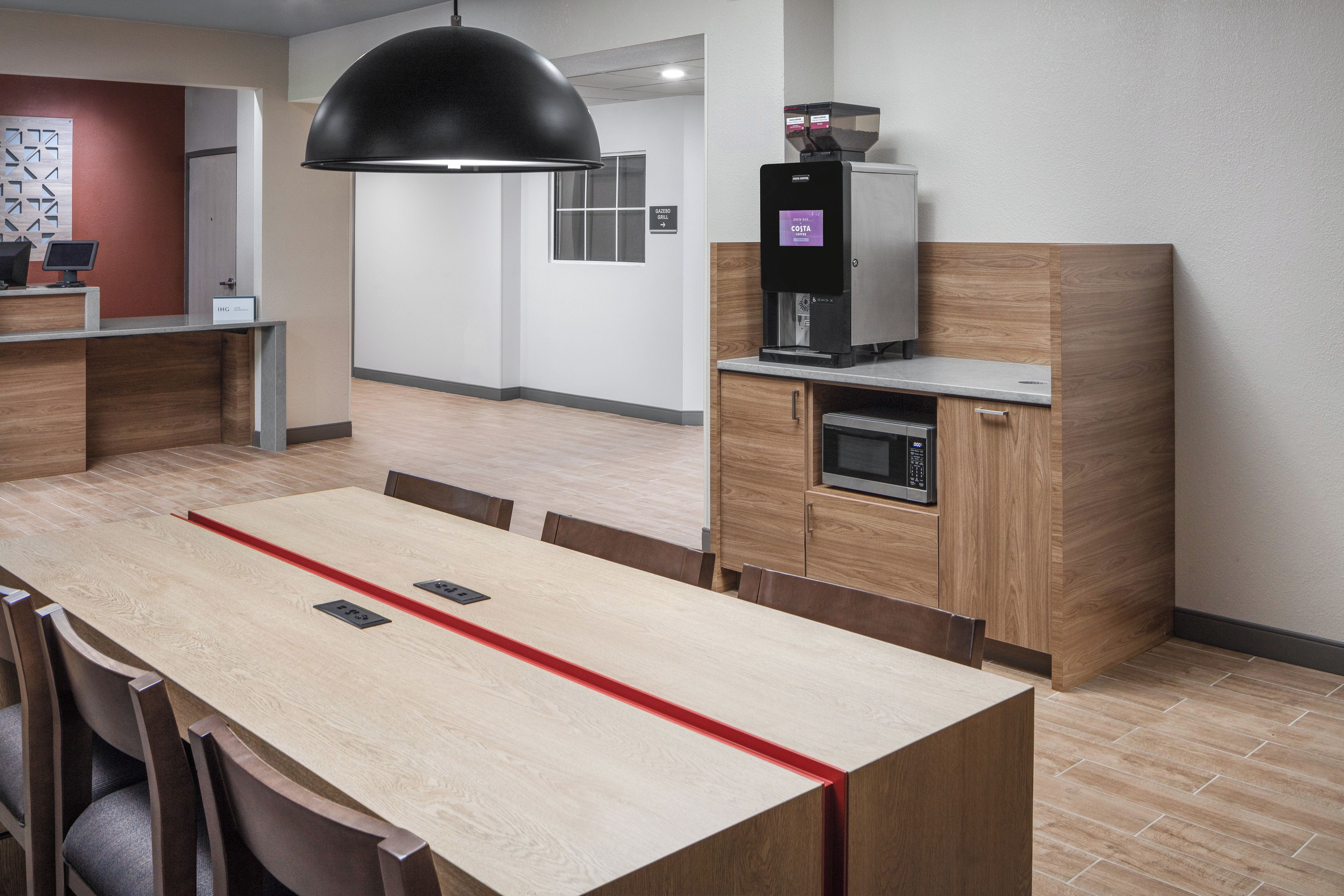 A modern kitchen with a coffee machine, a microwave, and a wooden cabinet.