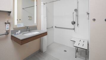 A modern bathroom with a sink, mirror, shower, and a small table.