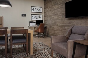 A modern office space with a conference table, chairs, a desk with a computer, and a television mounted on the wall. - Candlewood Suites St Robert by IHG (St. Robert)