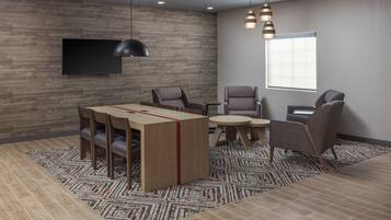 A modern room with a wooden wall, a flat-screen TV, a dining table with chairs, a small round table, and a patterned rug.