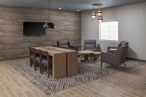 A modern room with a wooden wall, a flat-screen TV, a dining table with chairs, a small round table, and a patterned rug. - Candlewood Suites St Robert by IHG (St. Robert)