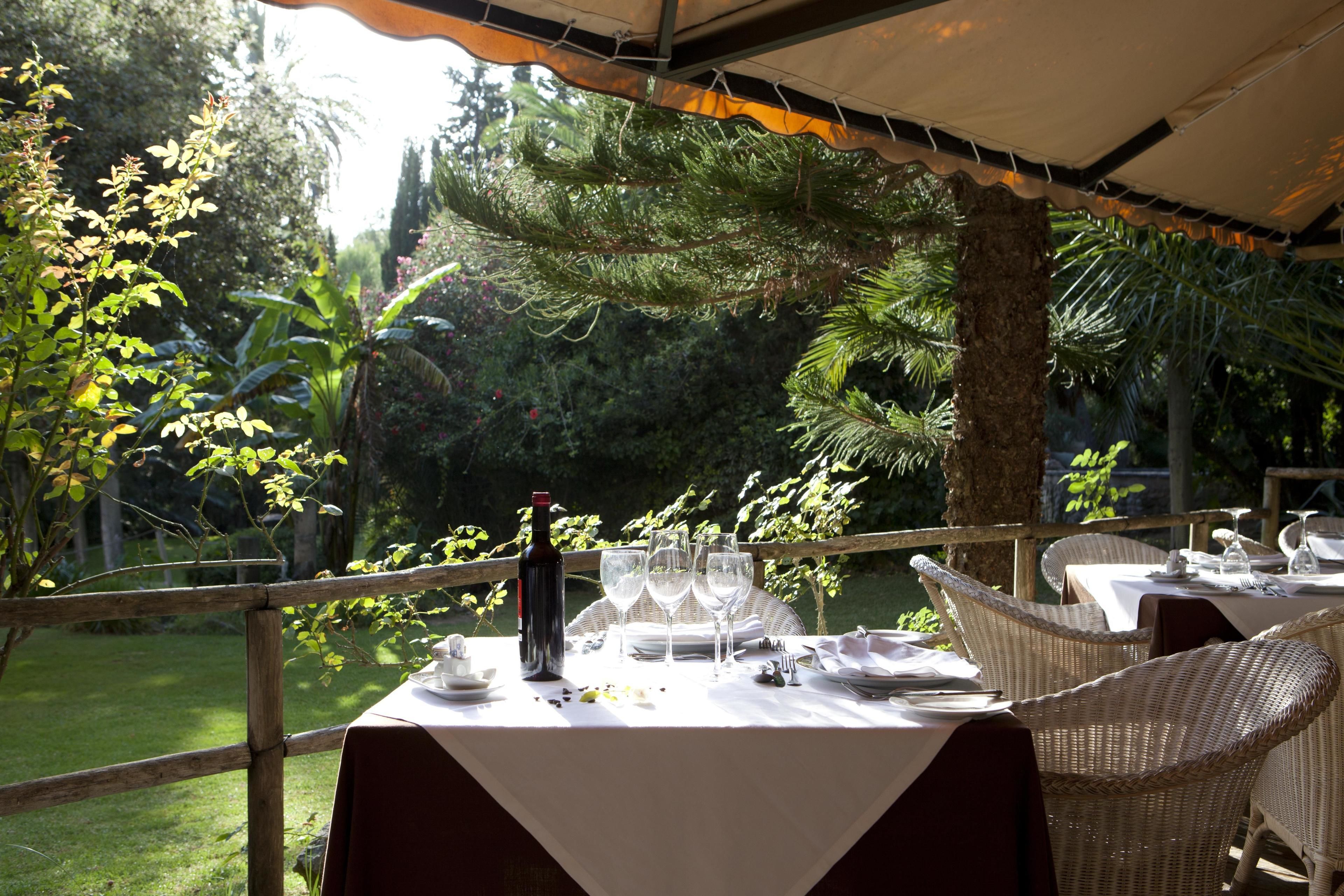 Un espace de restauration en plein air, avec des tables dressées pour le repas, entouré d’une végétation luxuriante et d’arbres.