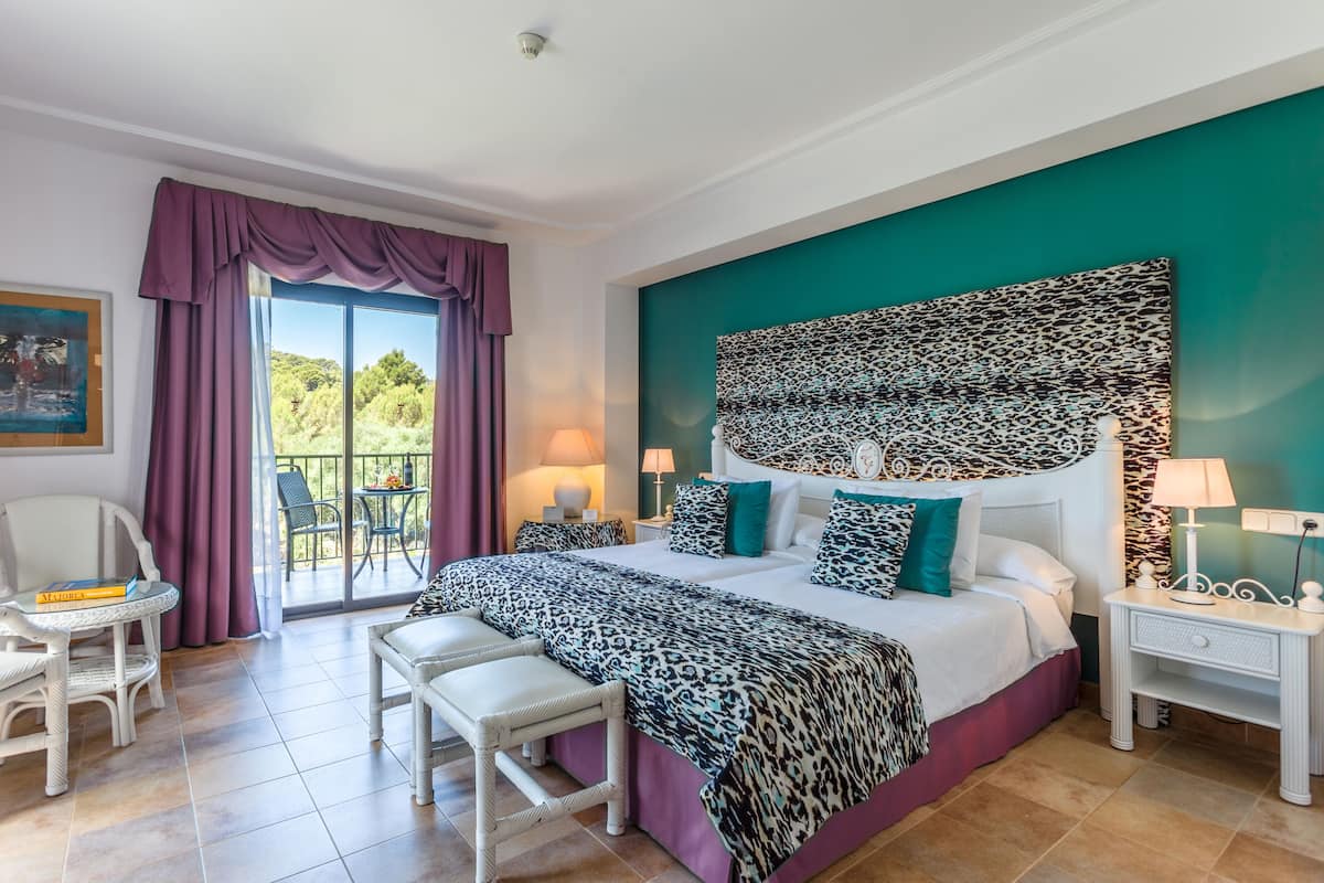 Un dormitorio con una cama grande, un cabecero con diseño estampado, un balcón con cortinas moradas y vistas a la vegetación.