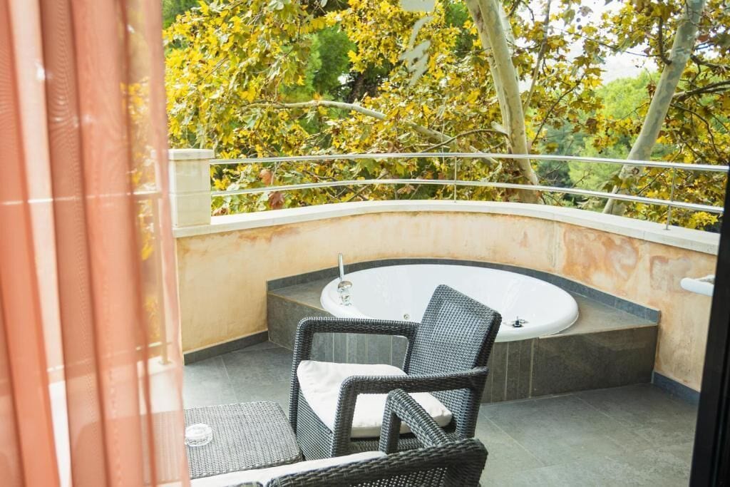 Ein Balkon mit einer runden Badewanne, Korbmöbeln und Blick auf Bäume.
