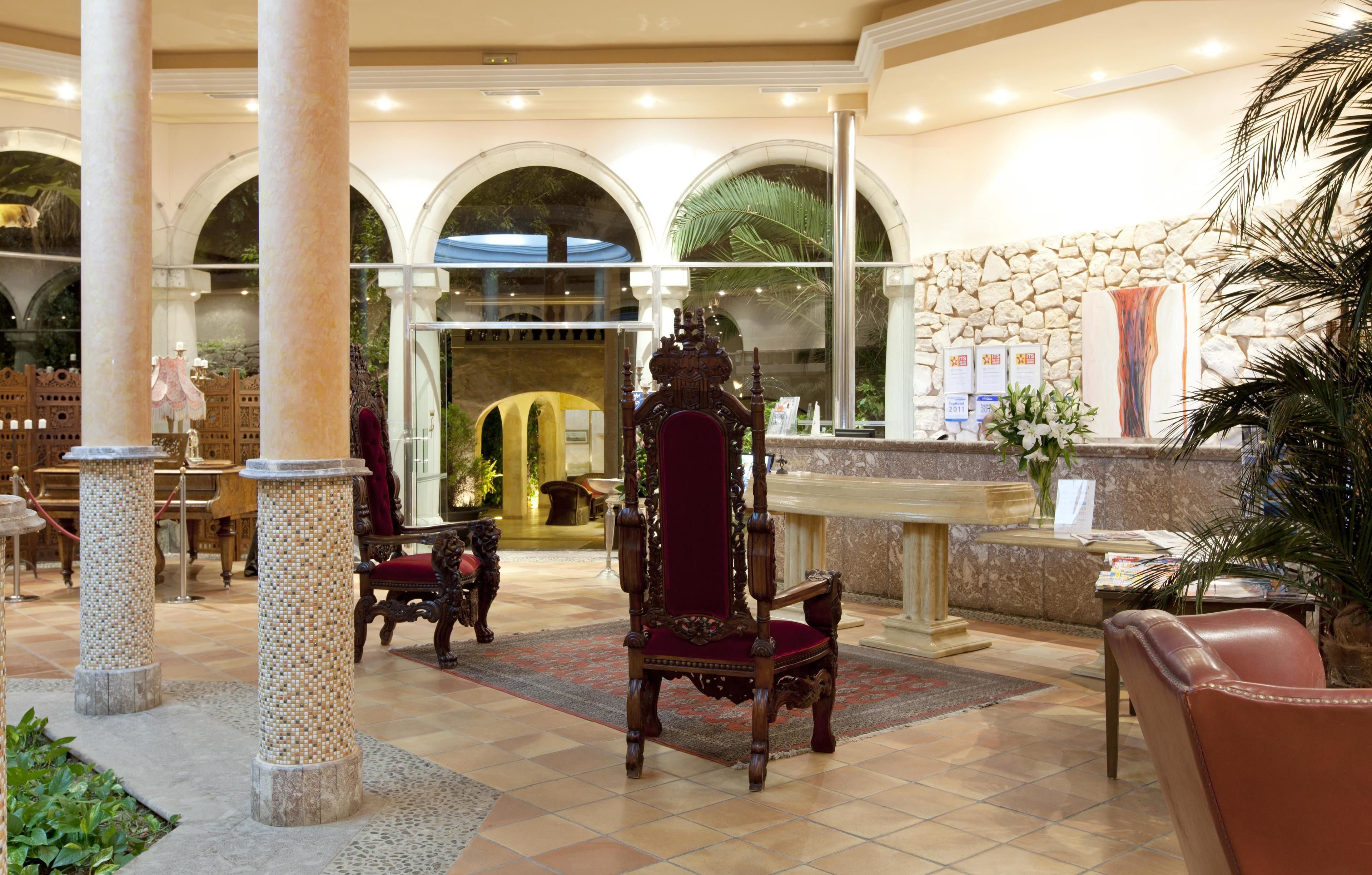 Una hall con una scrivania della reception, una grande poltrona decorata e un muro in pietra con un'ampia finestra.