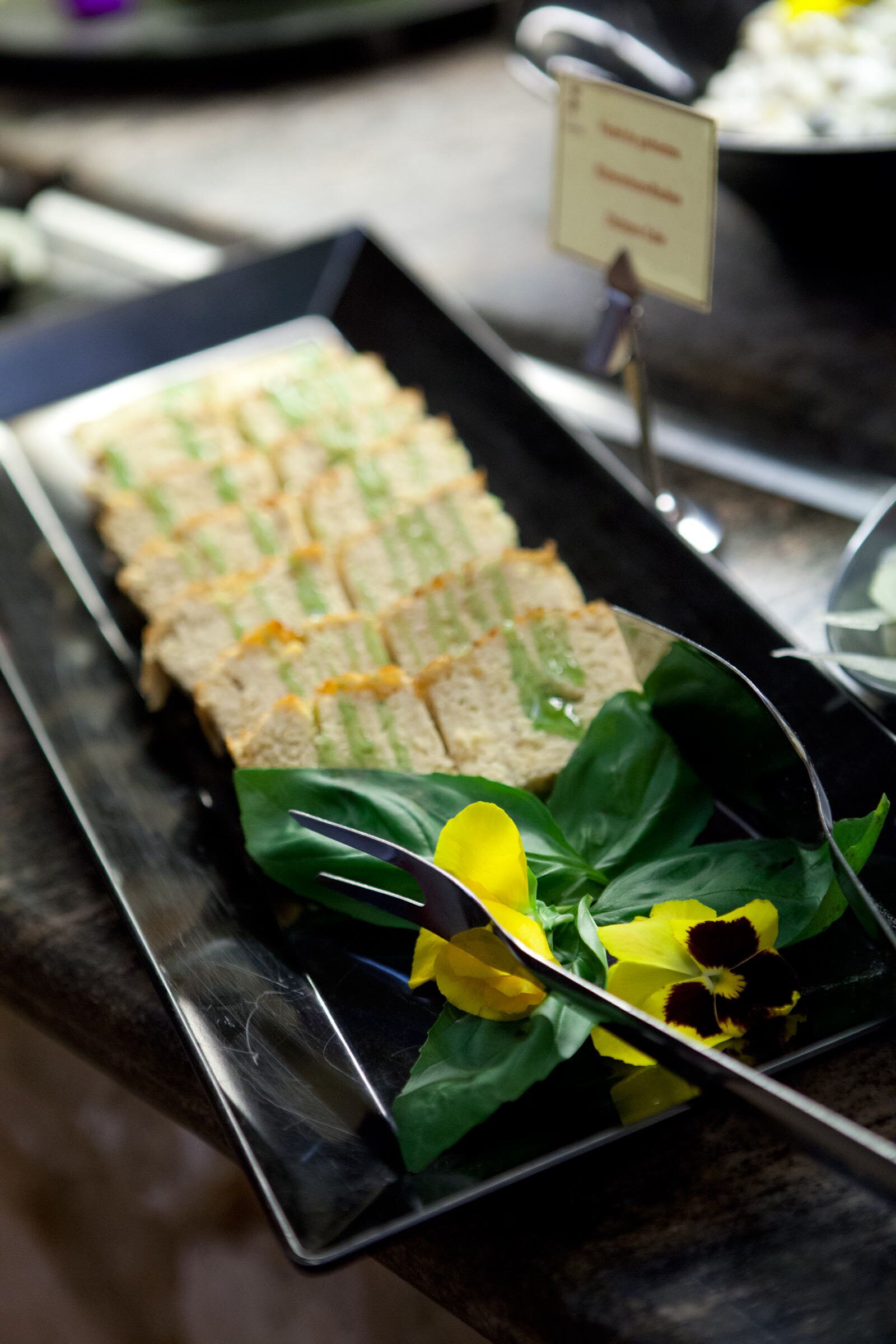 A tray of sandwiches with a sign, a glass of water, and some flowers on a table.