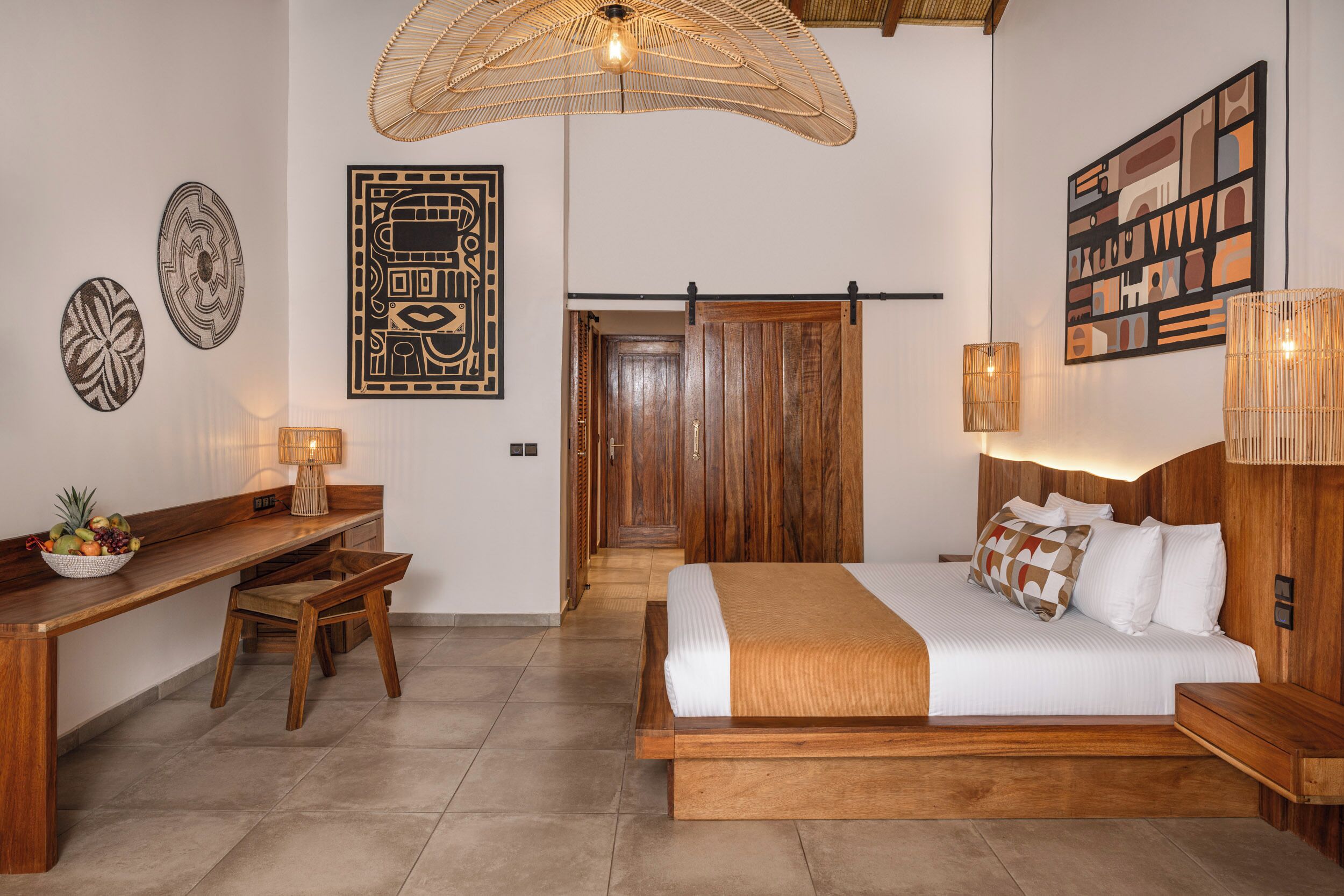 Un dormitorio con una cama de madera, un escritorio con una silla, un frutero y decoración en la pared.