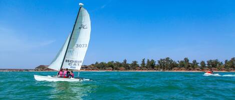 A sailboat with the number 3073 on its sail, sailing on turquoise waters with a beach and palm trees in the background.