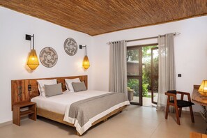 Une chambre à coucher avec un lit en bois, deux lampes fixées au mur, une petite table avec une lampe et une vue à travers une porte vitrée.