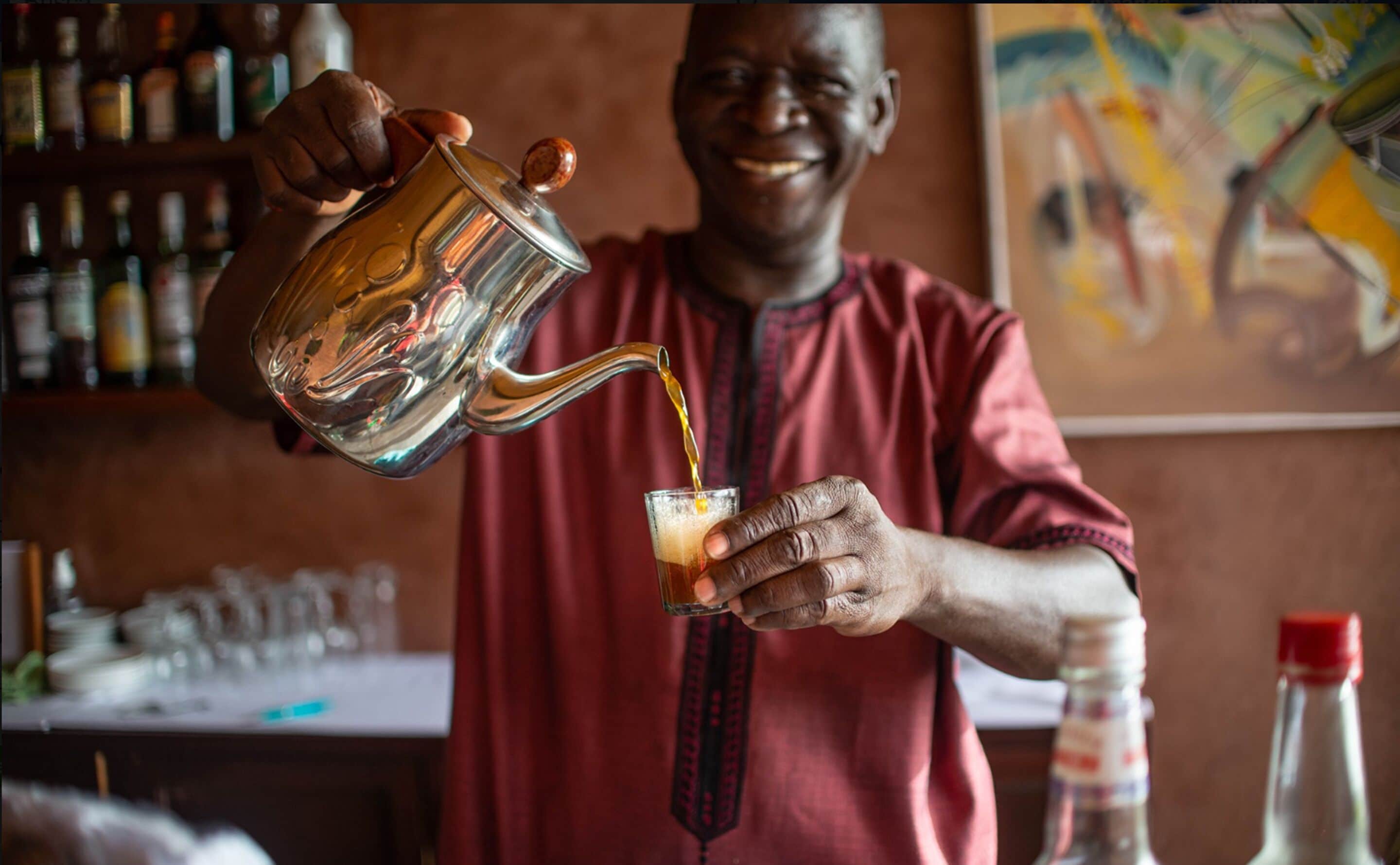 A person pouring a drink from a metal pitcher into a glass.