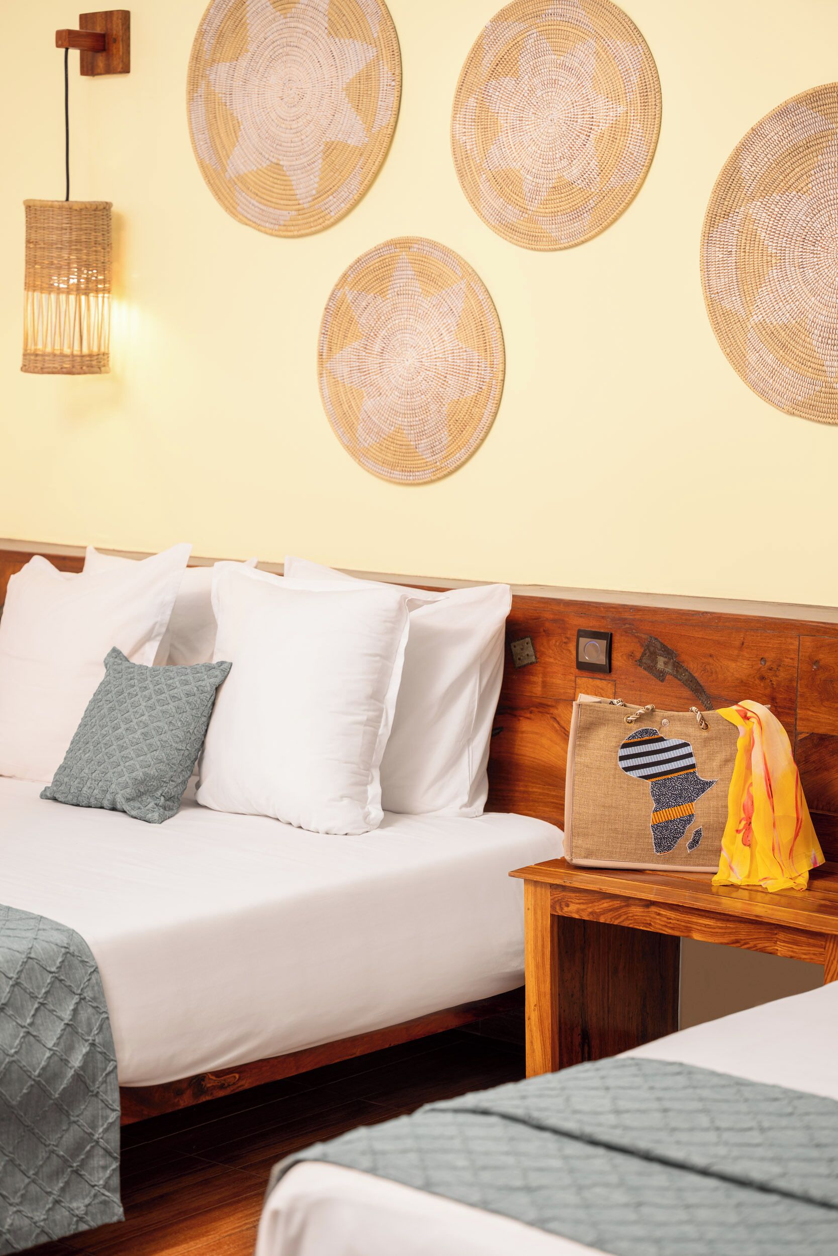 A hotel room with a wooden headboard, a bed with white bedding, a small wooden nightstand, and wall-mounted woven decor.