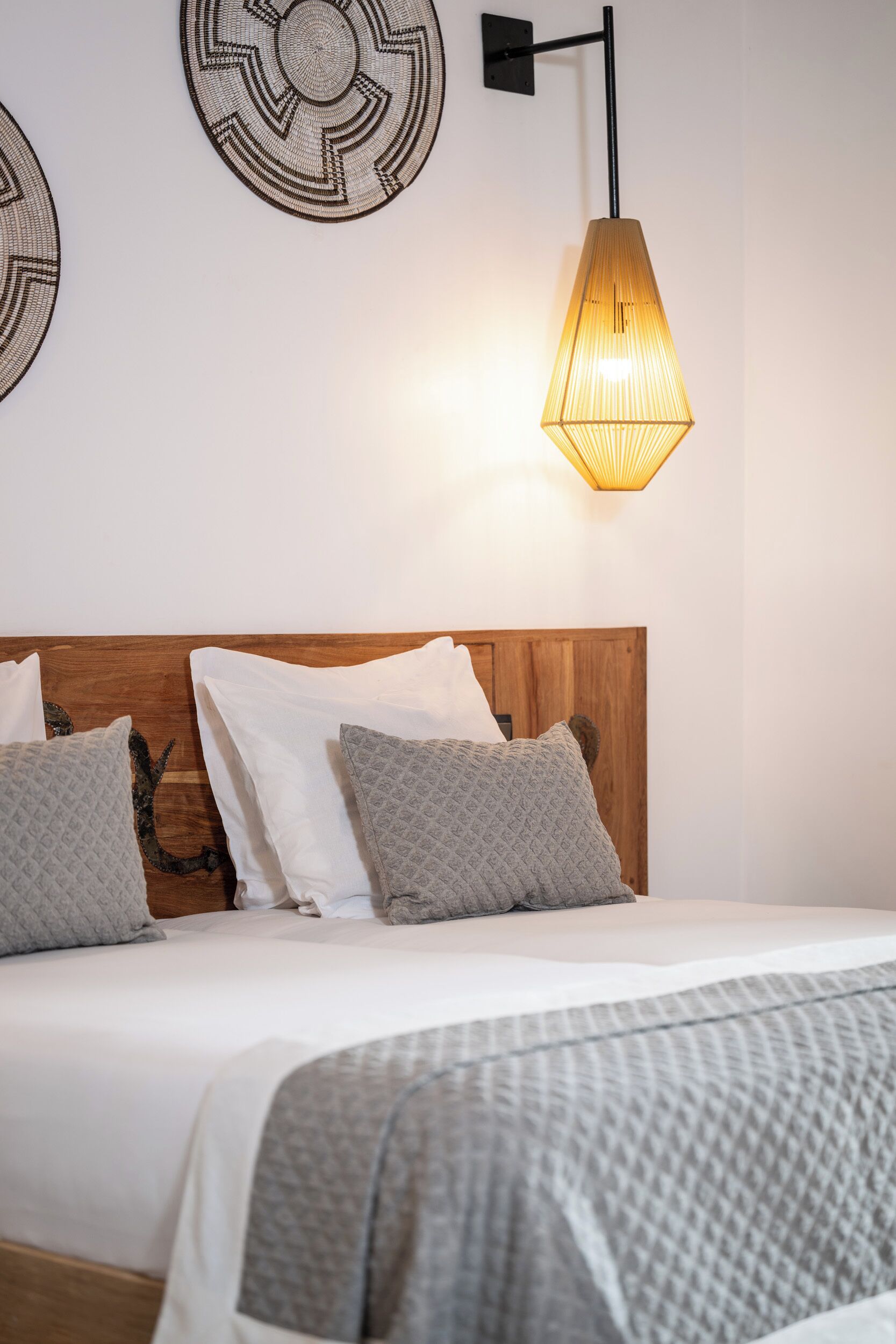 Un lit avec une tête de lit en bois, des oreillers à motifs gris et une couverture à texture.