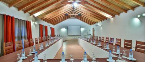 A conference room with a long table set for meetings, wooden ceiling beams, and red curtains.