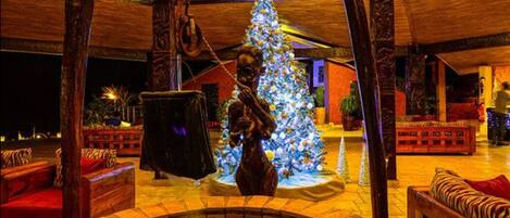 A warmly lit interior with a Christmas tree, wooden furniture, and a stone fireplace.