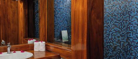 Un baño con tocador de madera, un lavamanos, un espejo y una pared de mosaico azul.