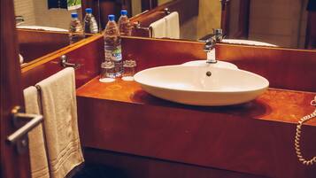 A hotel bathroom with a white sink, wooden vanity, and multiple bottles of water.