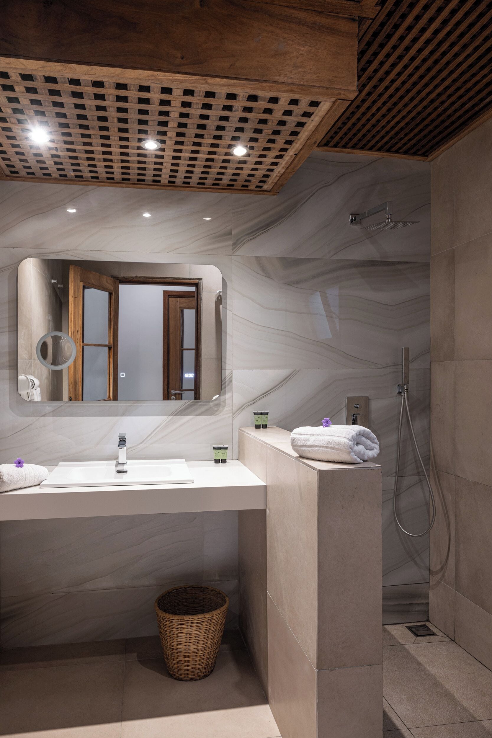 A modern bathroom with a marble vanity, a large mirror, a shower, and a wicker basket.