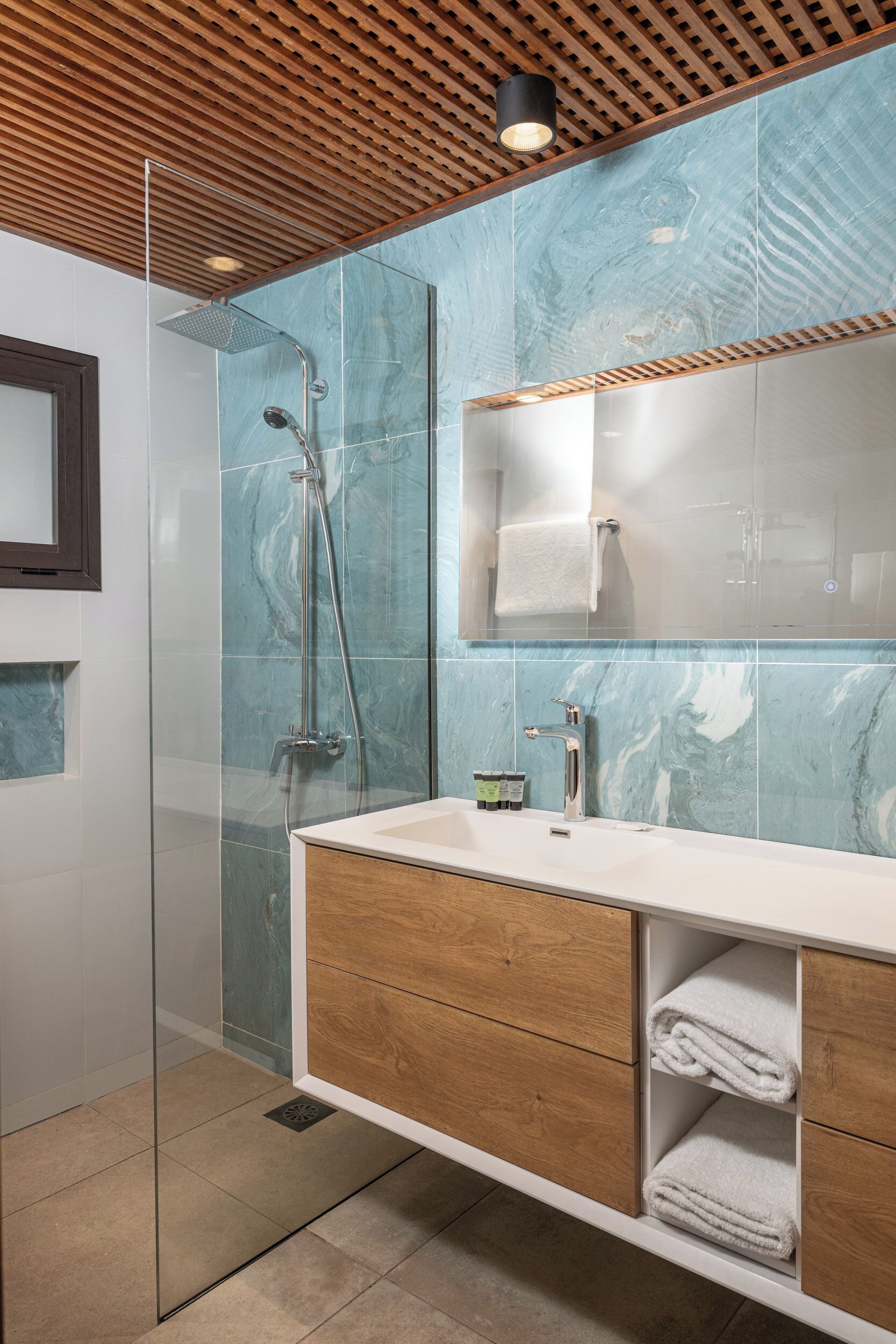 A modern bathroom with a glass shower enclosure, a wooden vanity, and a marble backsplash.