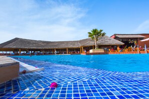 A swimming pool with a tiled deck, palm trees, and thatched-roof structures.
