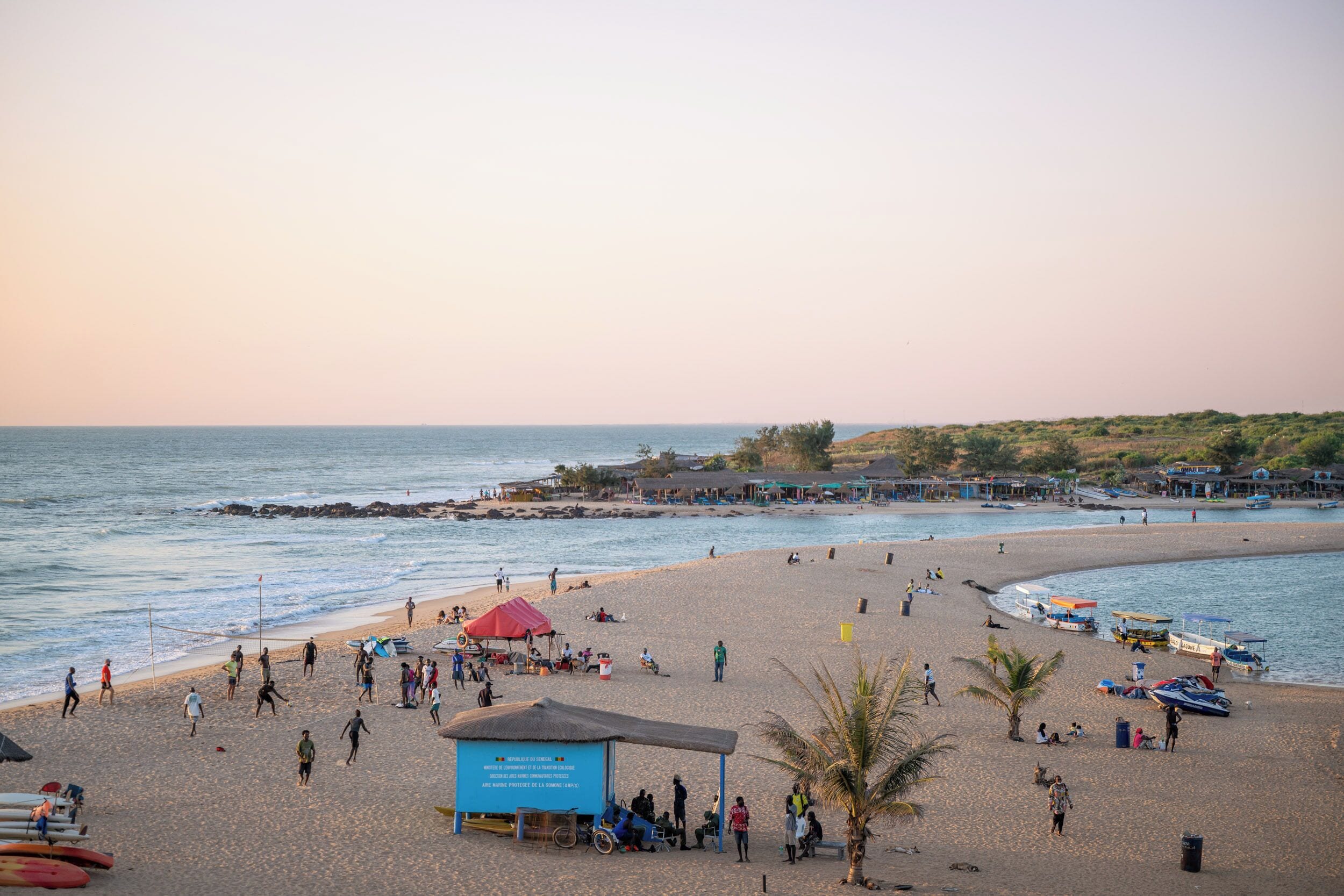 A beach with people, a blue shelter, and boats.