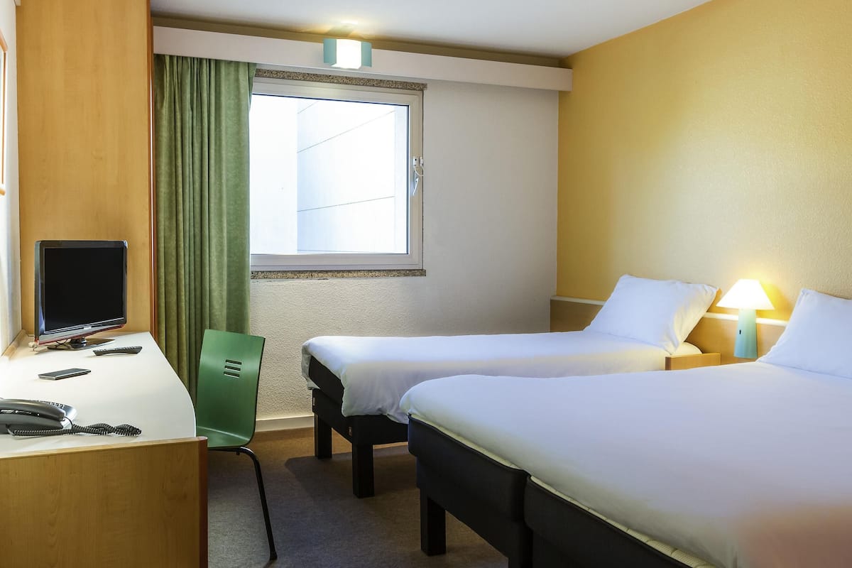 Une chambre d’hôtel avec deux lits, un bureau équipé d’un ordinateur, un téléphone et une chaise.
