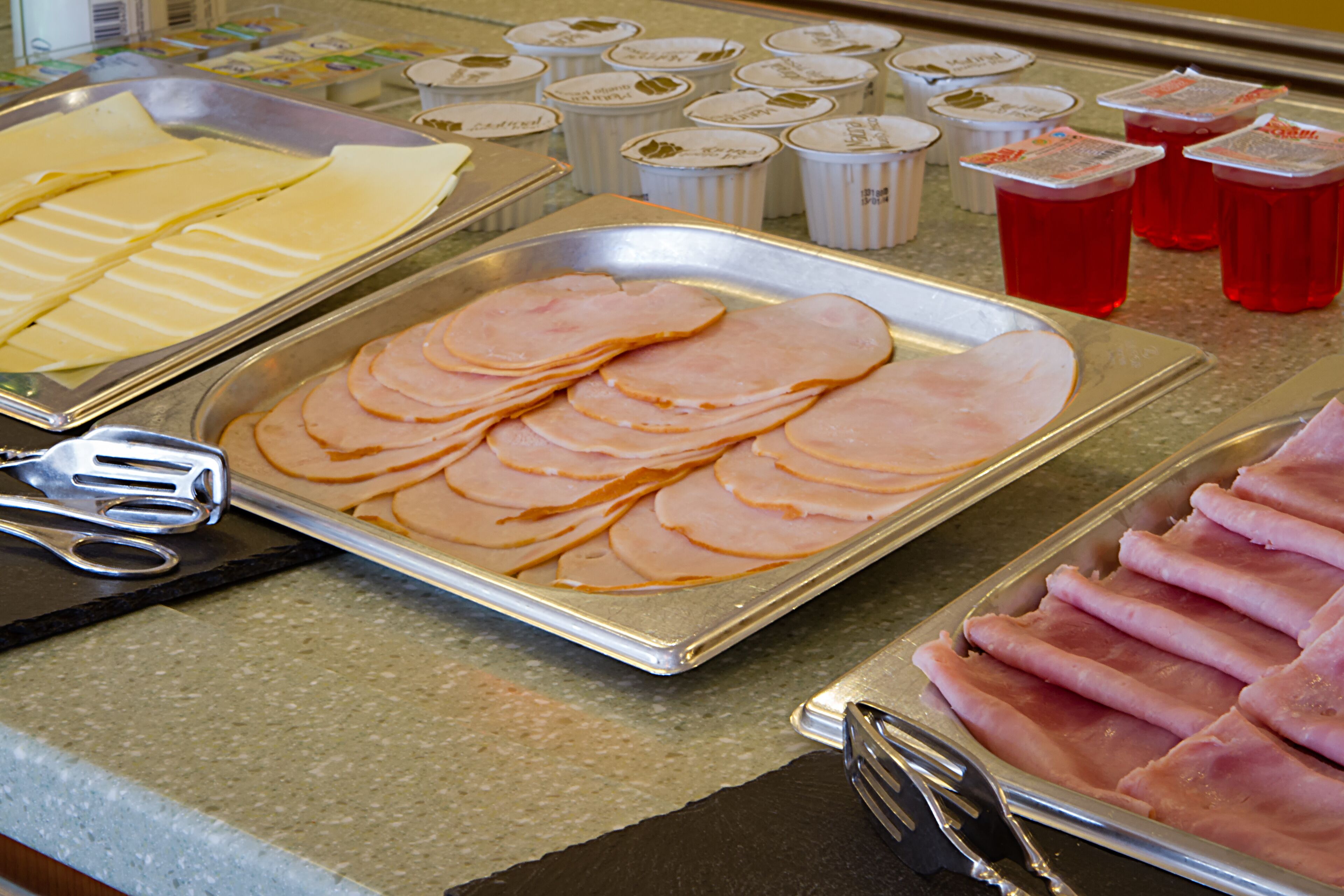 Buffet com fatias de presunto e queijo, além de várias opções de bebidas.