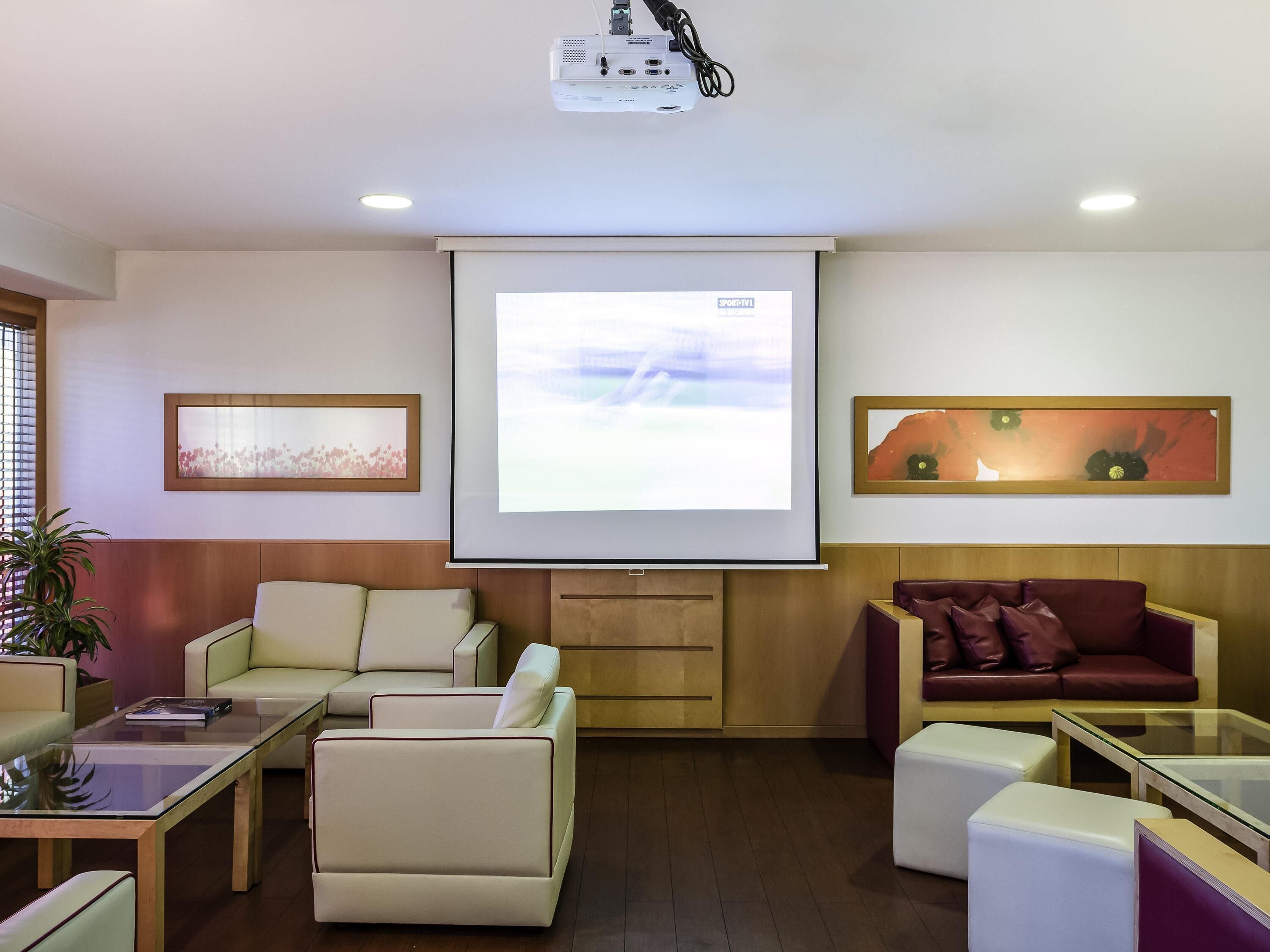 Um lounge moderno com uma tela grande, assentos confortáveis e um projetor.
