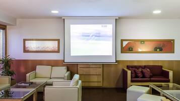Um lounge moderno com uma tela grande, assentos confortáveis e um projetor.
