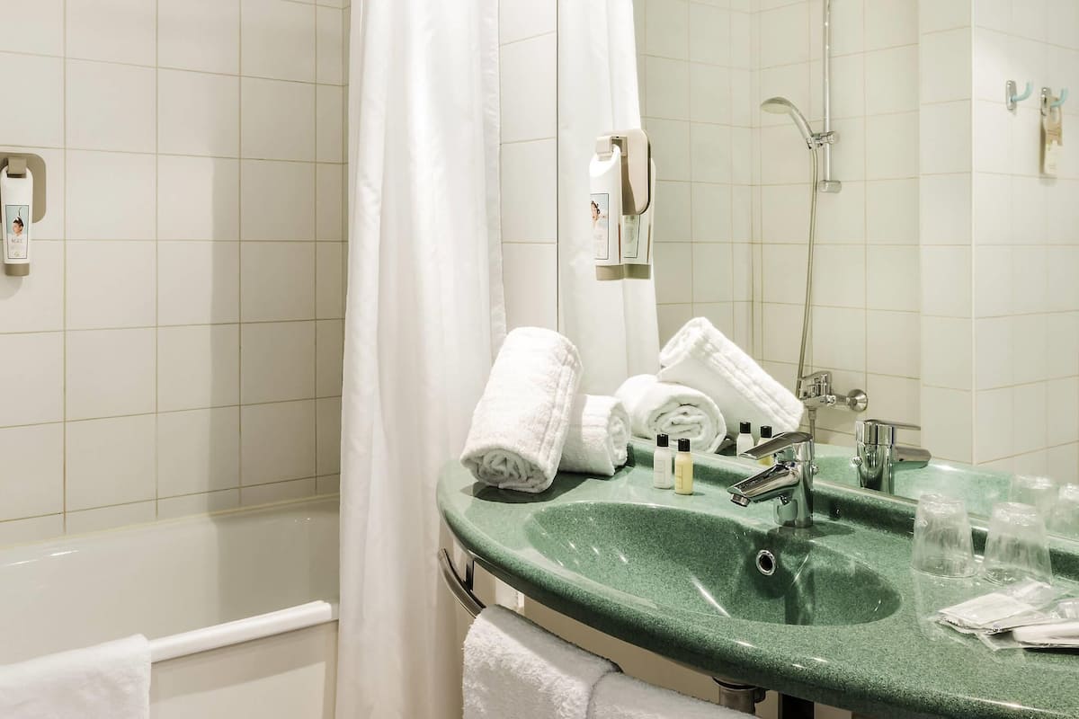A bathroom with a green sink, white towels, a shower, and a mirror.