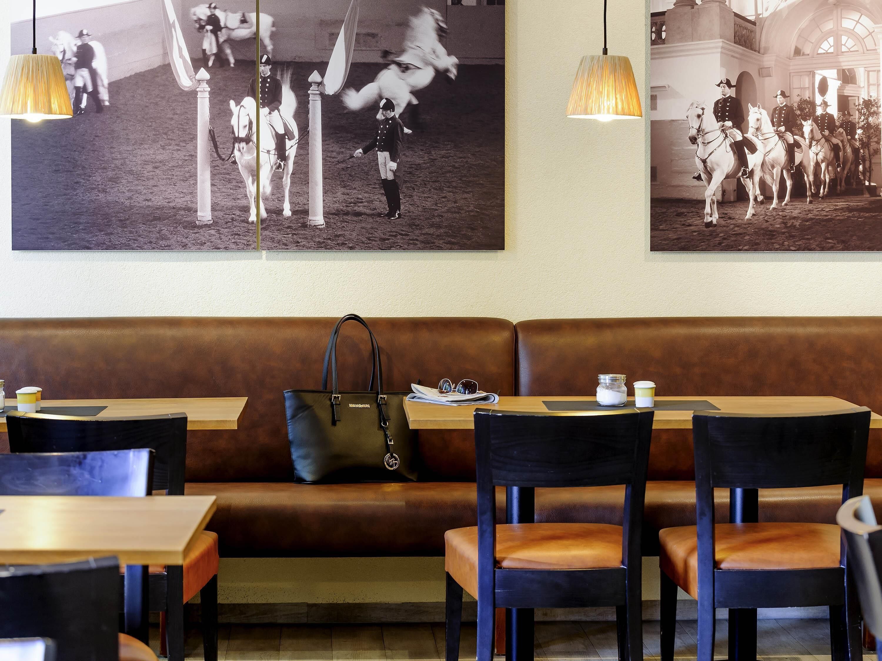 A restaurant interior with a brown leather booth, wooden tables, black chairs, and hanging pendant lights.