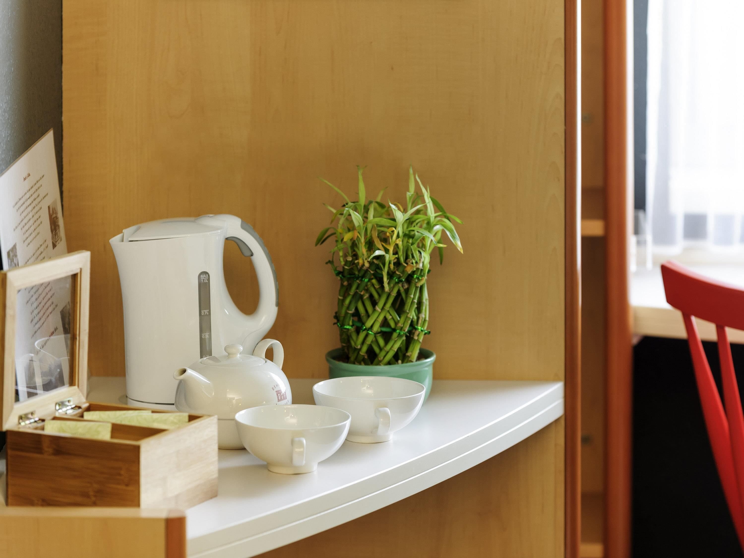 A kitchen counter with a white kettle, a green plant, and white cups and bowls.