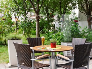 Una mesa redonda al aire libre con sillas de mimbre, una cerveza en un vaso y una pequeña planta en maceta.