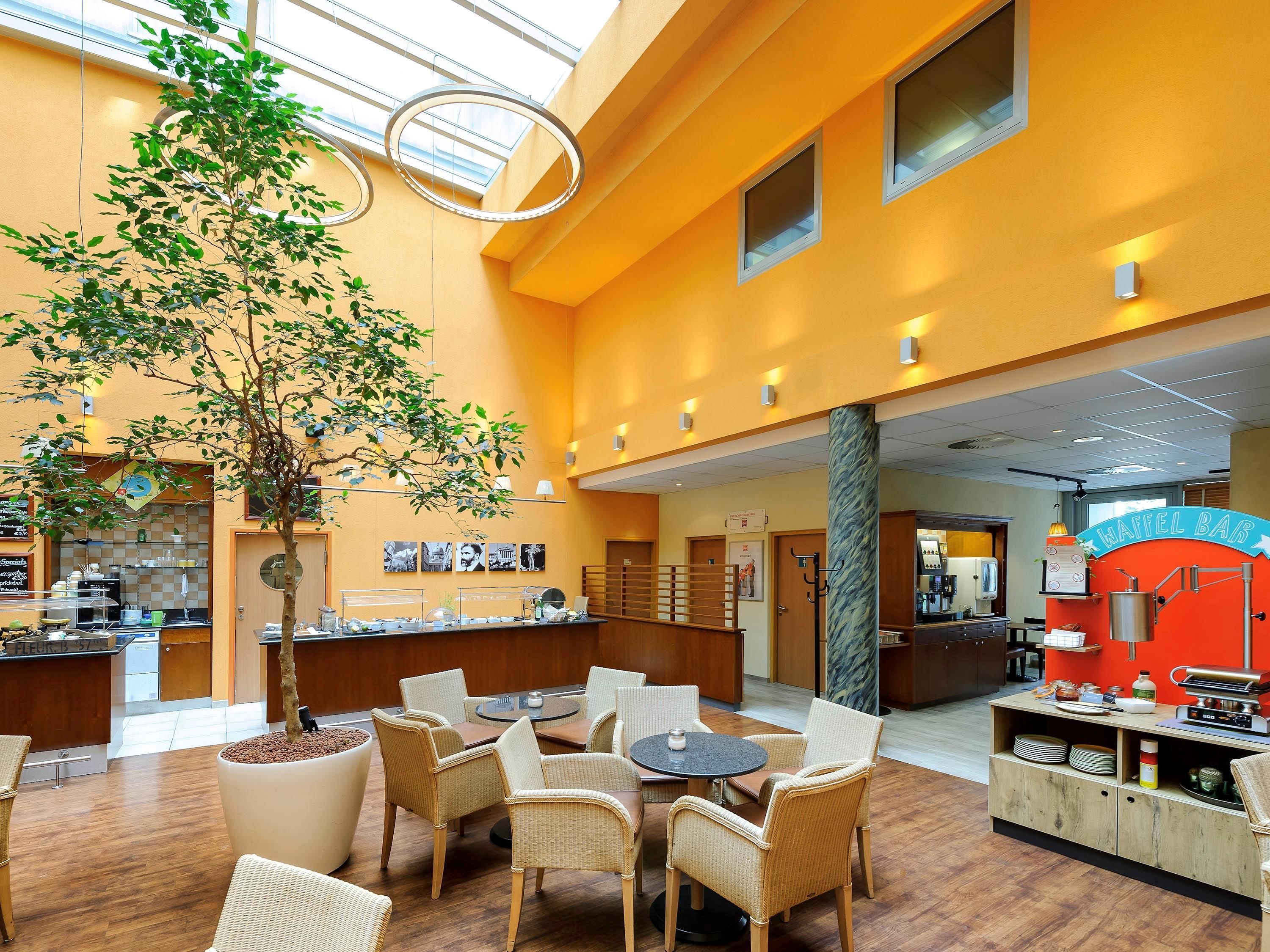 A hotel lobby with a central seating area, a waffle bar, and a large potted tree.