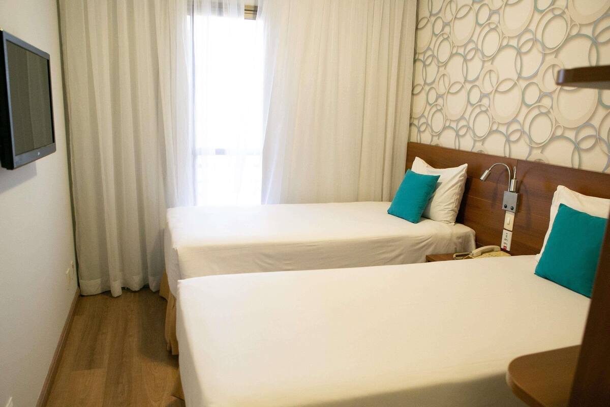 Habitación de hotel con dos camas, un televisor en la pared y una ventana con cortinas.