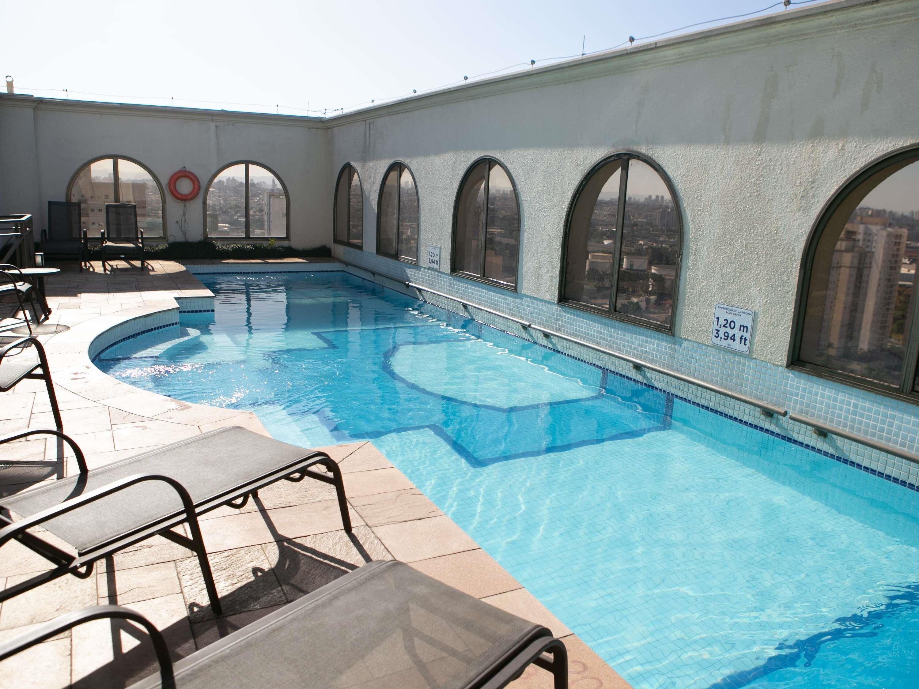 A rooftop swimming pool with clear blue water, surrounded by arched windows and outdoor seating.