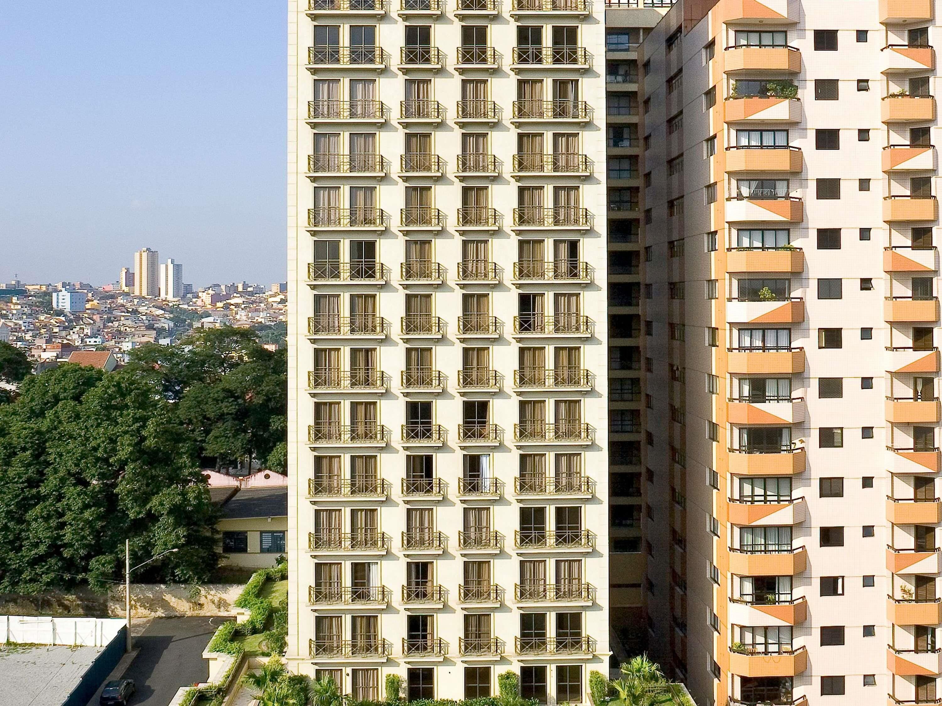 Un immeuble de grande hauteur doté de nombreux balcons, avec une vue sur la ville en arrière-plan et un ciel dégagé.