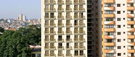 Un immeuble de grande hauteur doté de nombreux balcons, avec une vue sur la ville en arrière-plan et un ciel dégagé.