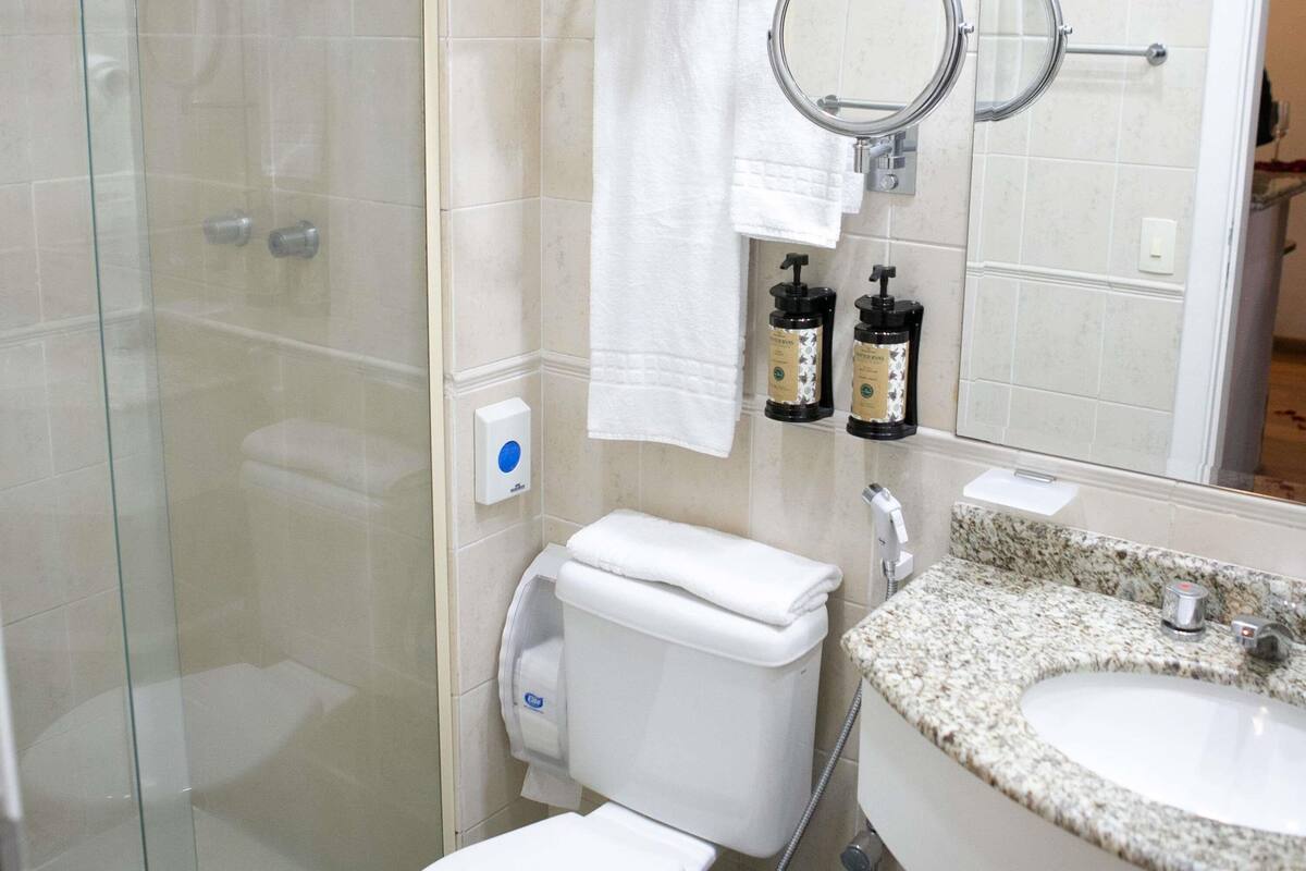 Un baño moderno con cabina de ducha de vidrio, inodoro, lavamanos con encimera de granito y espejo sobre el lavamanos.