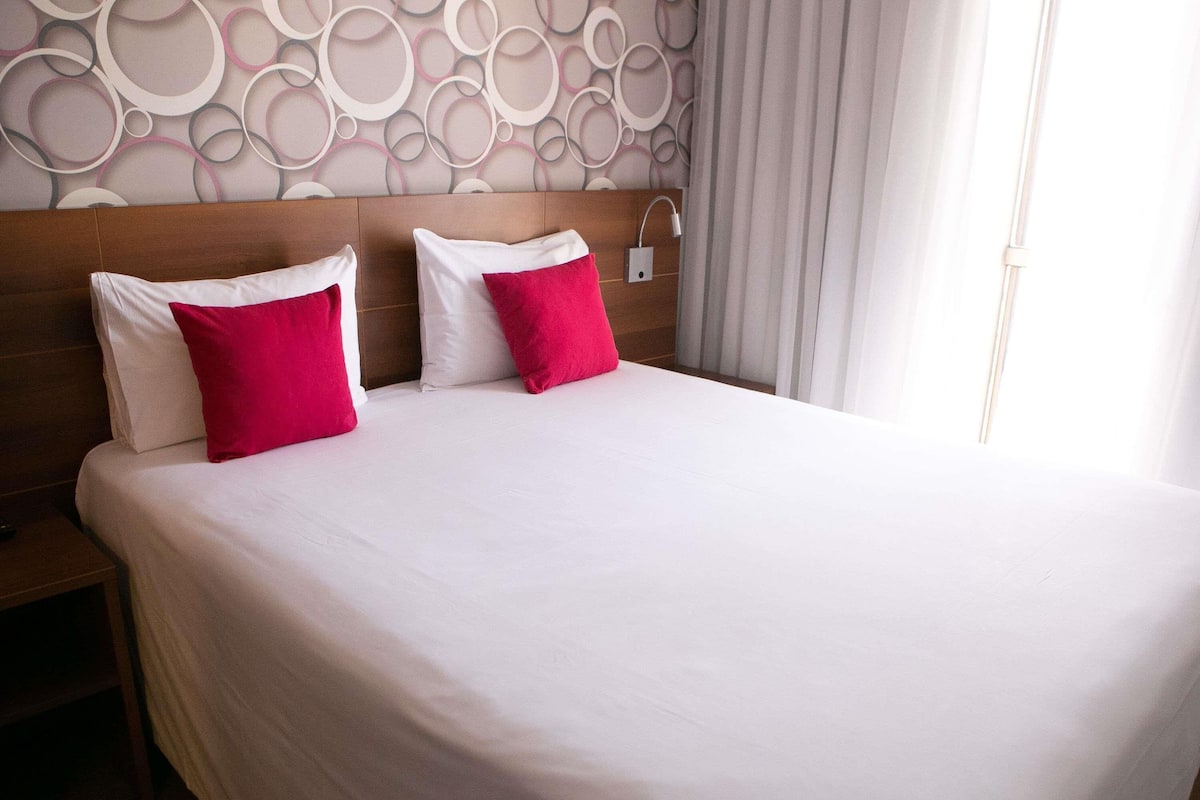 Una cama bien hecha con almohadas blancas y rojas, un cabecero de madera y una pared con diseños circulares.