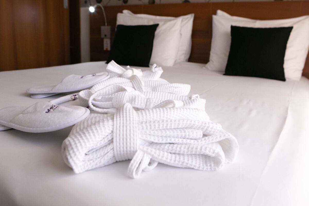 Una cama bien hecha con ropa blanca, un par de zapatillas y una toalla doblada.