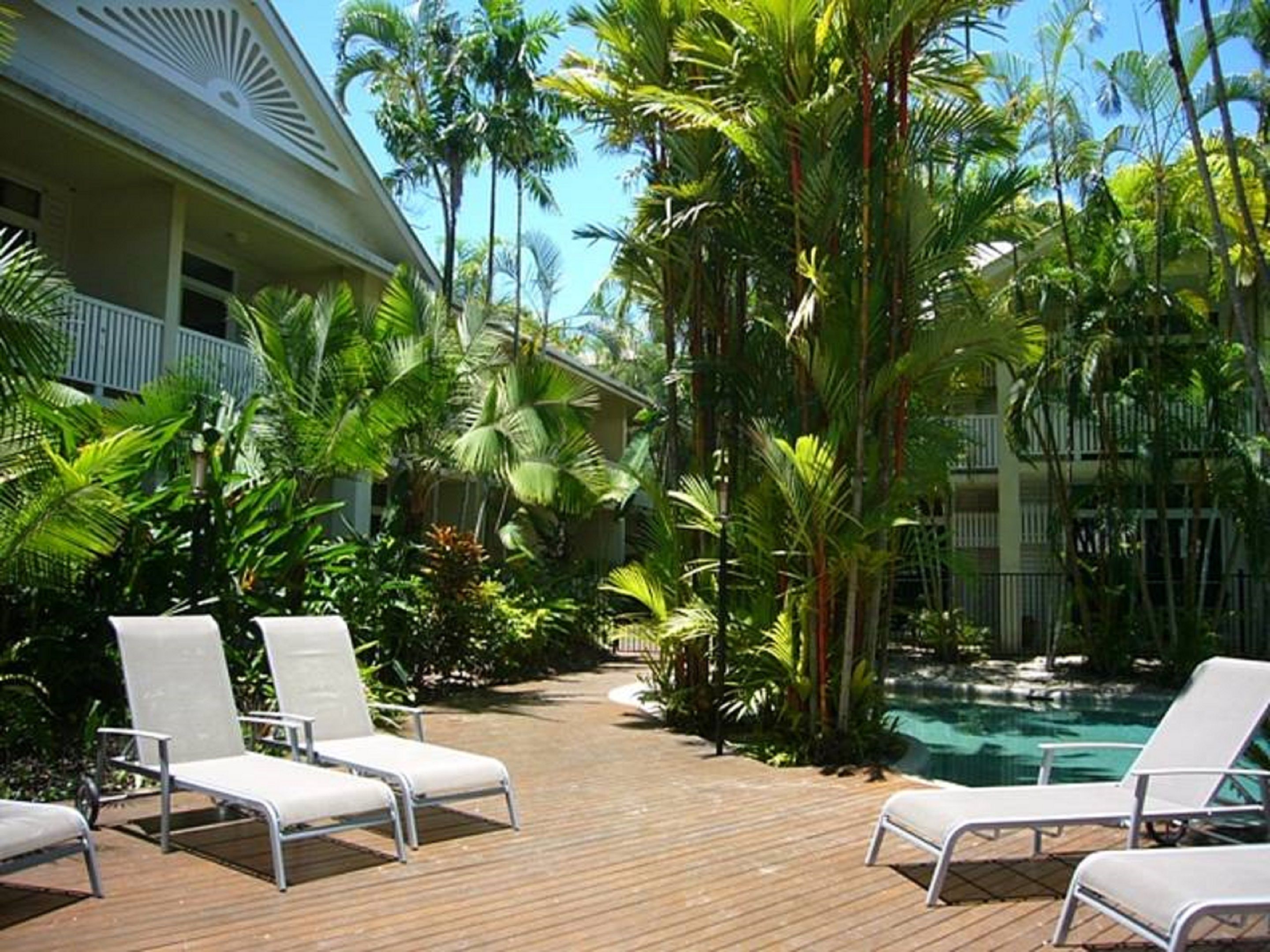 Uma área de piscina com espreguiçadeiras e plantas tropicais.