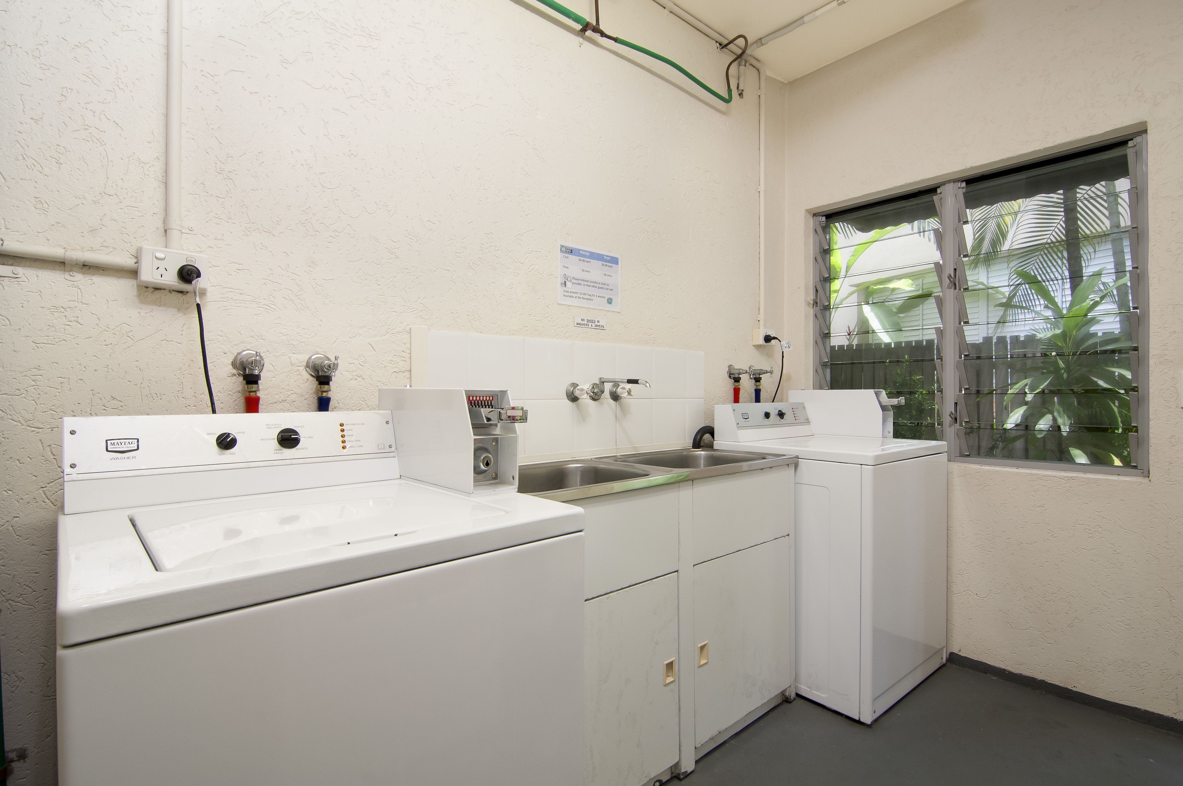 A laundry room with two washing machines, a sink, and a window with a view of palm trees.