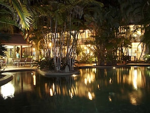 A nighttime pool area with palm trees and a building in the background. - Port Douglas Retreat (Port Douglas)