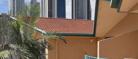 Um edifício com vários andares, uma varanda curva, palmeiras e um horizonte urbano ao fundo.
