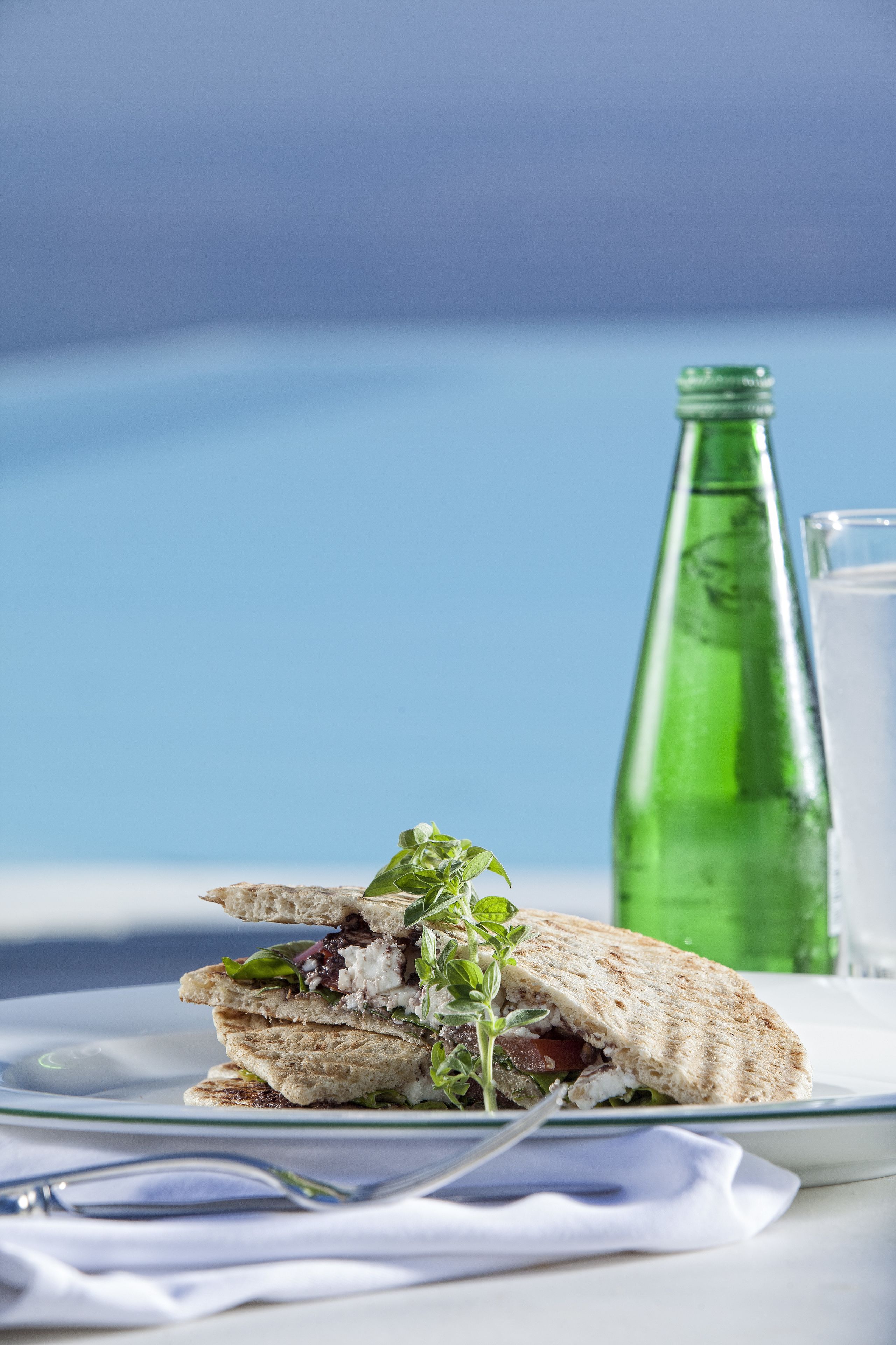 A sandwich on a plate with a green bottle and a glass of water in the background.