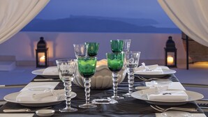 A table set for dining with green glassware and white plates, overlooking a scenic view. - The Tsitouras Collection Hotel (Santorini)