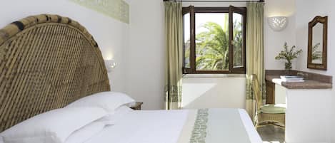 Ein Hotelzimmer mit einem großen Bett, einem Fenster mit Vorhängen, einem Nachttisch, einem Sessel und einem Spiegel.