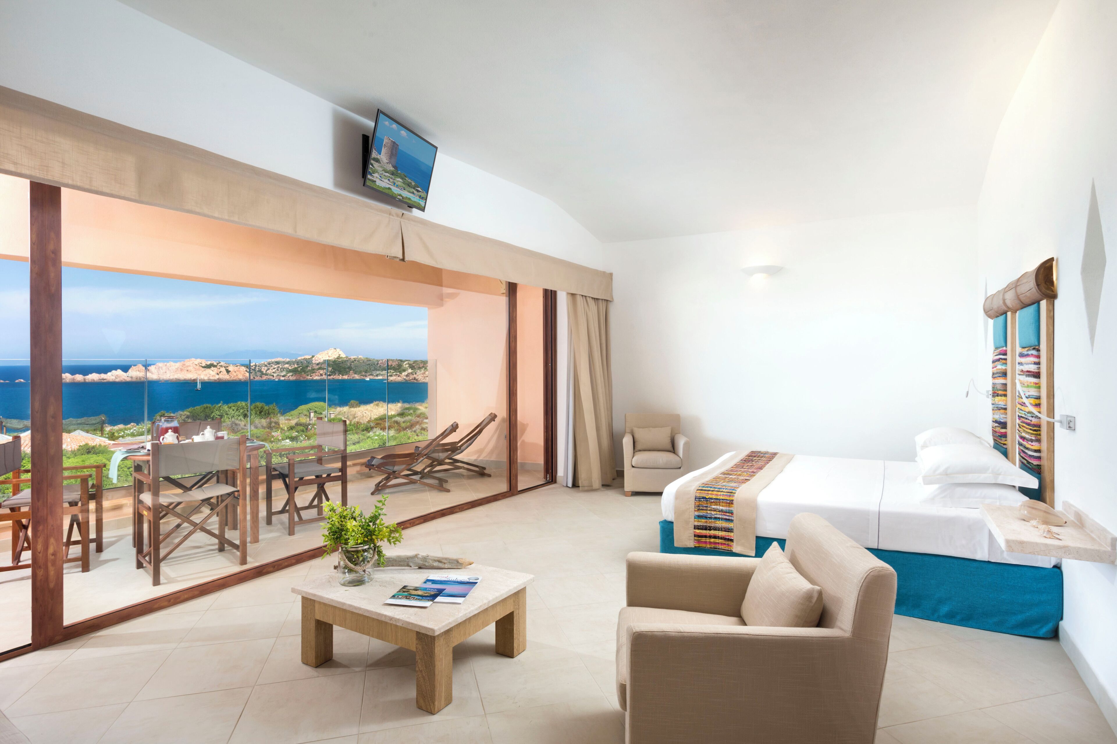 A hotel room with a balcony, a bed, a sofa, a coffee table, and a TV.
